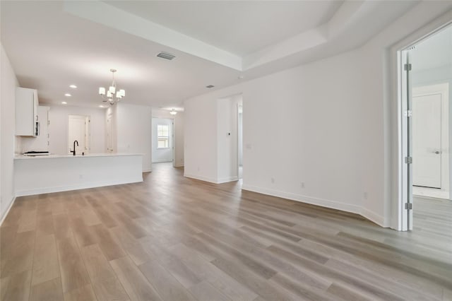 unfurnished living room featuring light hardwood / wood-style floors, sink, and an inviting chandelier