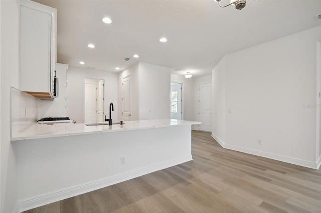 kitchen with kitchen peninsula, sink, white cabinets, and light wood-type flooring