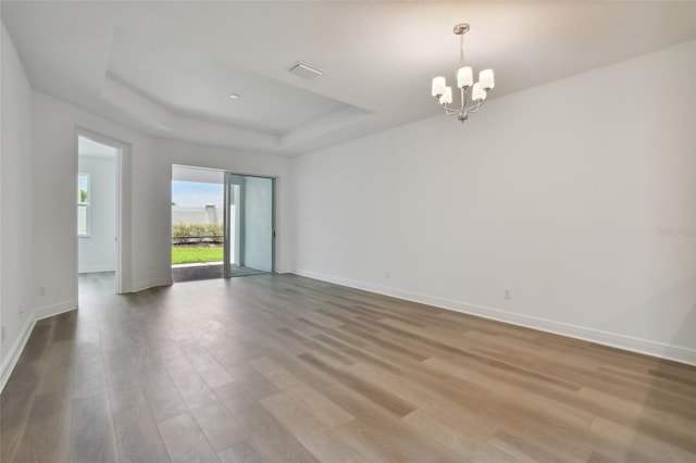 unfurnished room featuring a notable chandelier, a raised ceiling, visible vents, wood finished floors, and baseboards