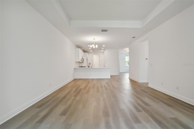 unfurnished living room featuring a notable chandelier, a sink, visible vents, baseboards, and light wood-type flooring