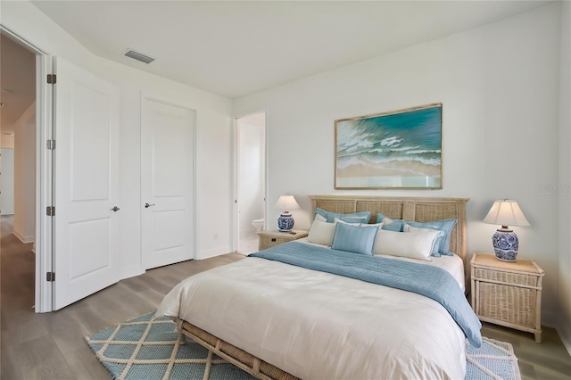 bedroom with ensuite bath, wood finished floors, visible vents, and baseboards