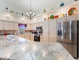 kitchen with decorative backsplash, light stone countertops, appliances with stainless steel finishes, and an inviting chandelier