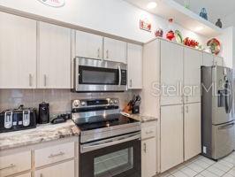 kitchen featuring decorative backsplash, light stone countertops, light tile patterned floors, white cabinetry, and stainless steel appliances