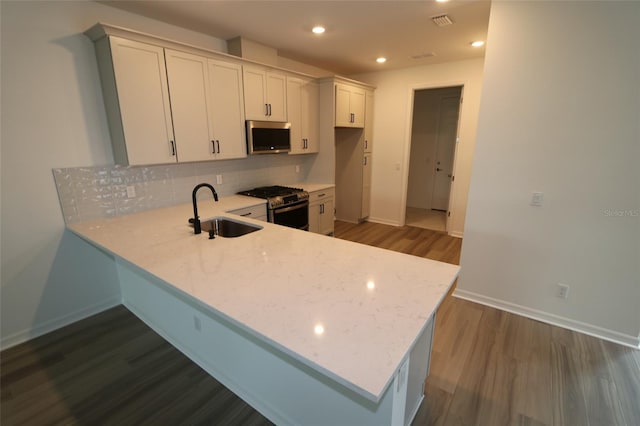 kitchen featuring dark hardwood / wood-style floors, white cabinets, sink, backsplash, and gas range oven