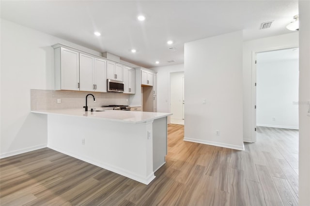 kitchen with light hardwood / wood-style flooring, white cabinets, kitchen peninsula, and backsplash