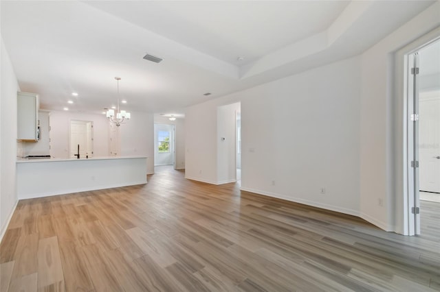 unfurnished living room featuring a notable chandelier, light wood-type flooring, and a tray ceiling