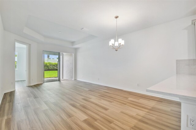 unfurnished dining area featuring light wood-type flooring, a raised ceiling, and an inviting chandelier