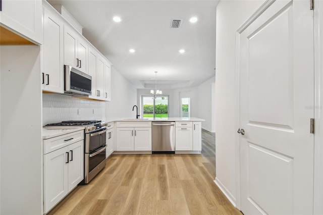 kitchen featuring tasteful backsplash, stainless steel appliances, hanging light fixtures, light hardwood / wood-style floors, and kitchen peninsula