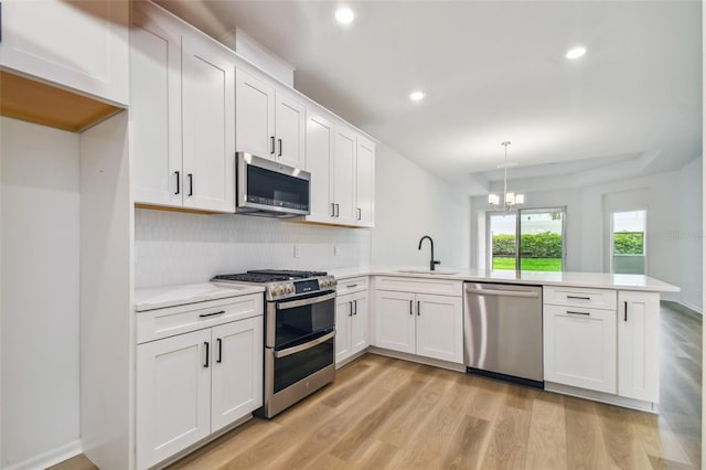 kitchen with decorative light fixtures, stainless steel appliances, sink, light hardwood / wood-style floors, and kitchen peninsula