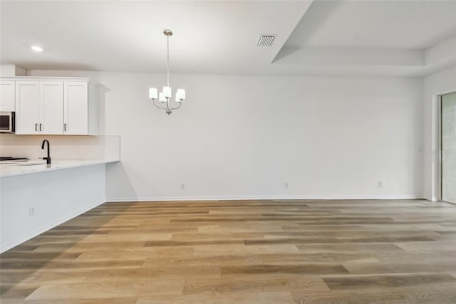 unfurnished dining area featuring an inviting chandelier, sink, a tray ceiling, and hardwood / wood-style floors