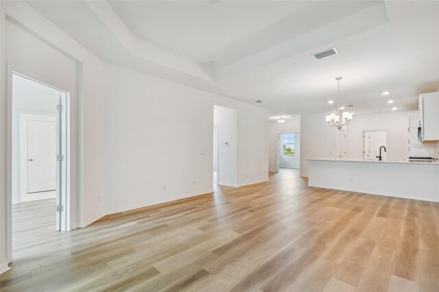 unfurnished living room with an inviting chandelier, light wood-type flooring, and a raised ceiling