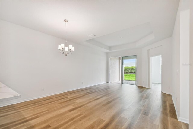 empty room featuring an inviting chandelier, wood-type flooring, and a tray ceiling