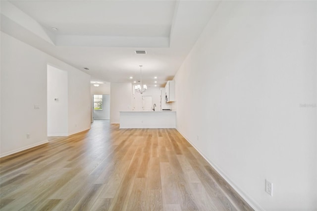 unfurnished living room with sink, a chandelier, and light wood-type flooring