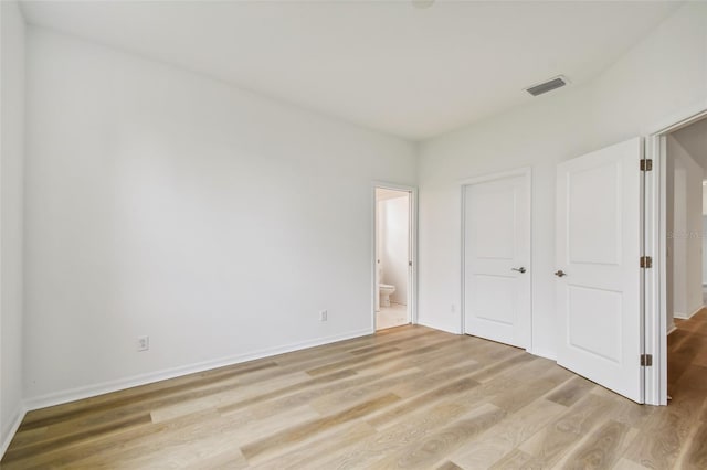 unfurnished bedroom featuring ensuite bath and light hardwood / wood-style floors