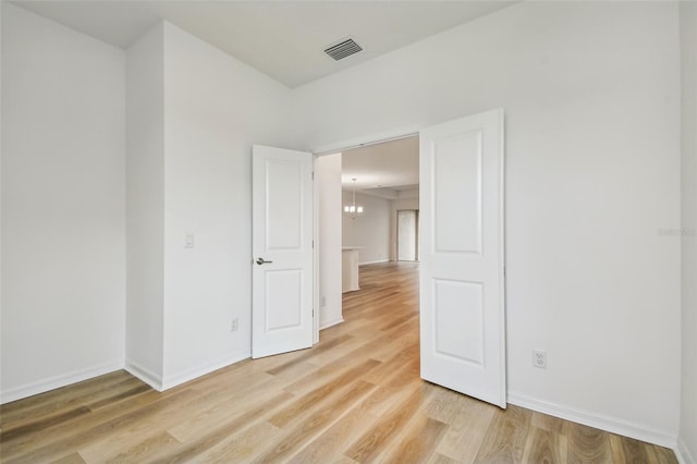 spare room with light wood-type flooring and an inviting chandelier