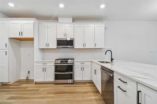 kitchen with sink, light wood-type flooring, light stone counters, and stainless steel appliances