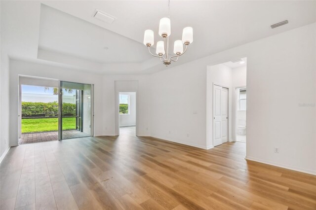 empty room with a tray ceiling, a chandelier, and light hardwood / wood-style flooring