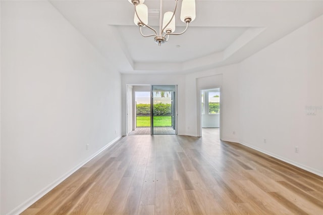 empty room featuring an inviting chandelier, wood-type flooring, and a tray ceiling