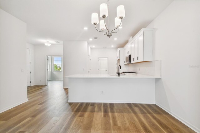 kitchen featuring a chandelier, kitchen peninsula, white cabinets, pendant lighting, and wood-type flooring