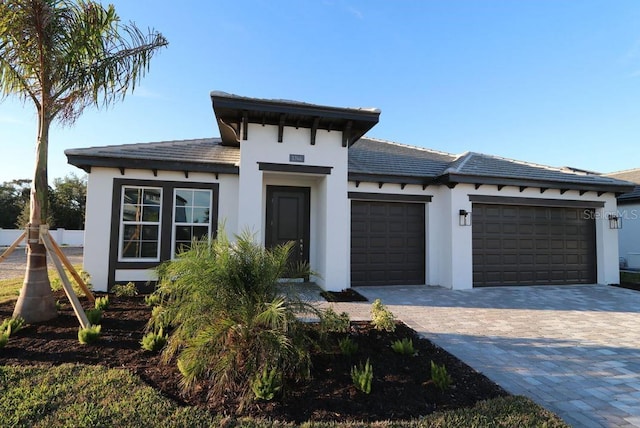 prairie-style home with decorative driveway, an attached garage, and stucco siding