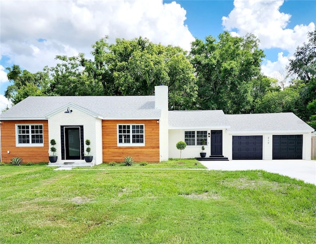 view of front facade featuring an attached garage, driveway, a chimney, and a front yard