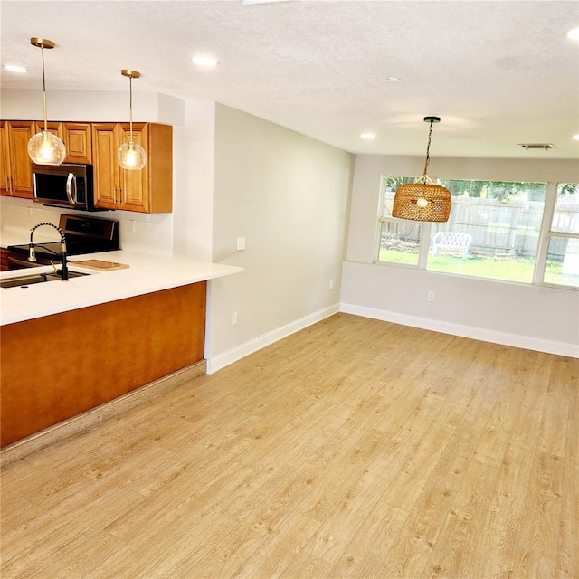 kitchen featuring stove, stainless steel microwave, brown cabinets, and light wood finished floors