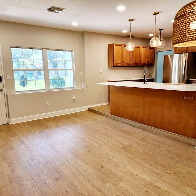 kitchen featuring light wood-type flooring, freestanding refrigerator, brown cabinetry, light countertops, and hanging light fixtures