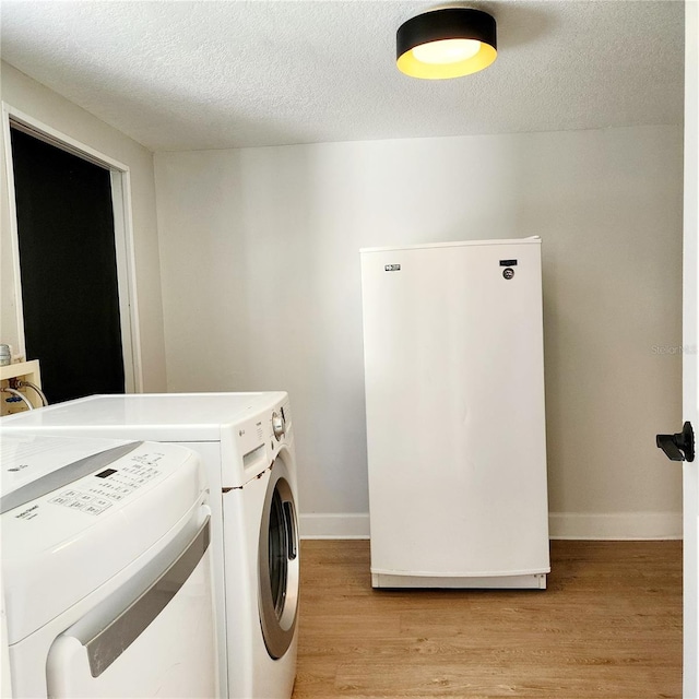 laundry area with washer and clothes dryer, a textured ceiling, light wood-type flooring, and baseboards