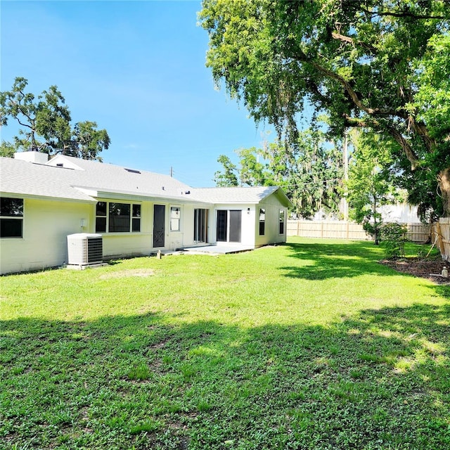 back of house with central air condition unit, a yard, a shingled roof, and fence