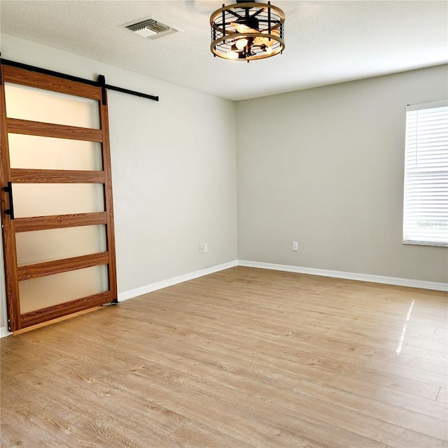 unfurnished room with visible vents, a barn door, baseboards, and light wood finished floors