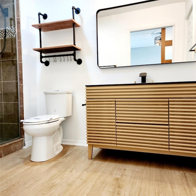 full bath with tiled shower, toilet, baseboards, and wood finished floors