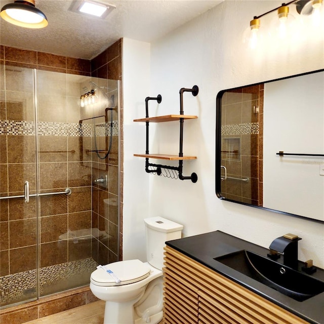 full bath with toilet, a stall shower, vanity, and a textured ceiling