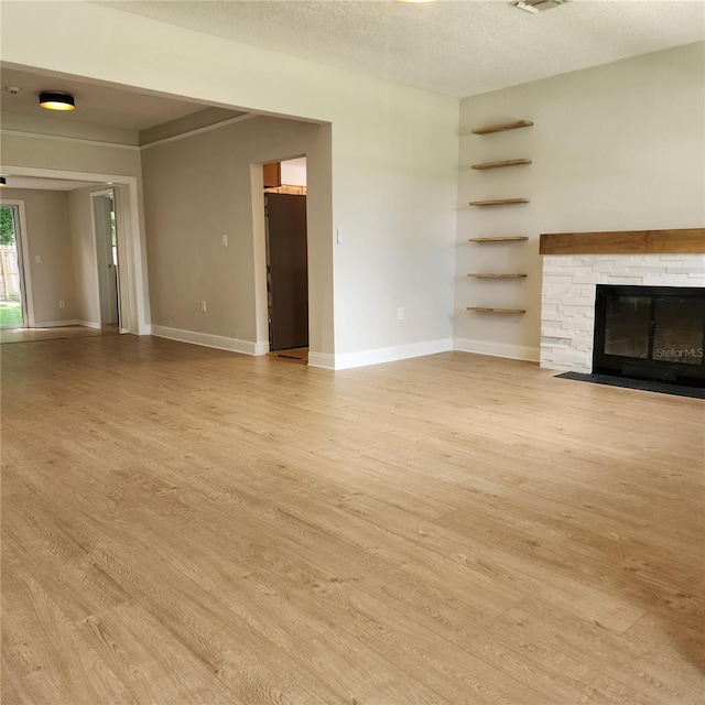 unfurnished living room featuring a stone fireplace, light hardwood / wood-style flooring, and a textured ceiling