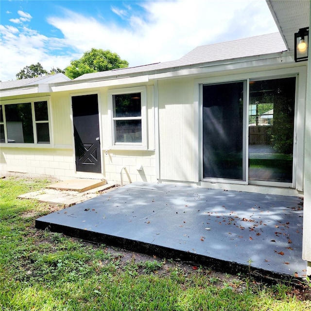 back of house featuring roof with shingles, concrete block siding, and a patio area