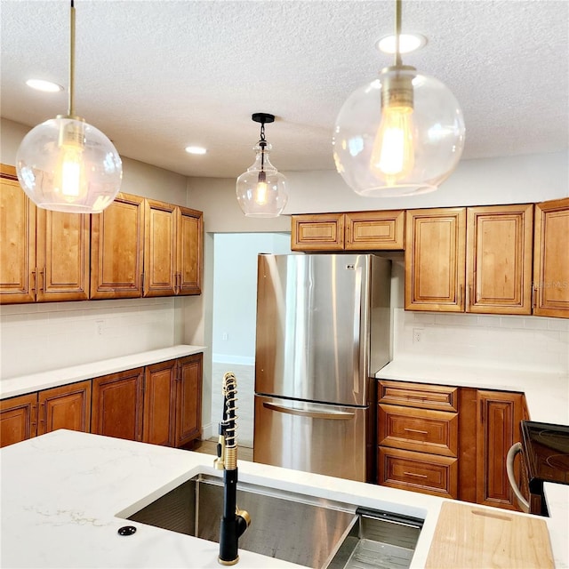 kitchen with brown cabinets, freestanding refrigerator, a sink, decorative light fixtures, and tasteful backsplash