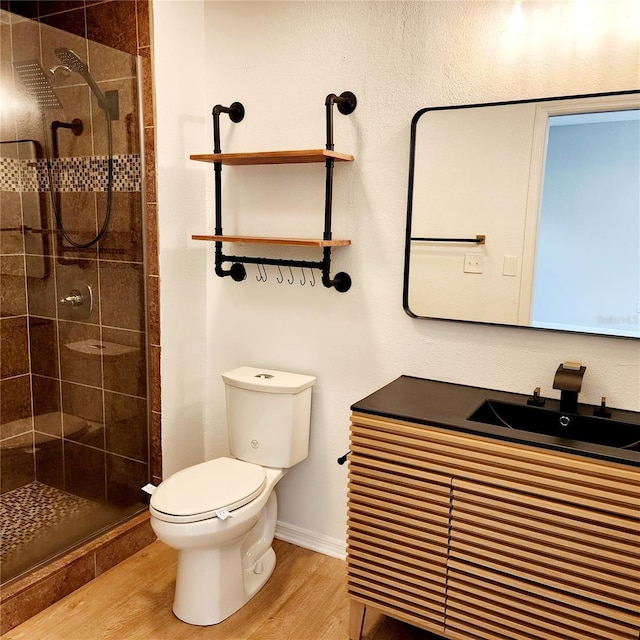 bathroom with baseboards, toilet, a stall shower, wood finished floors, and a sink