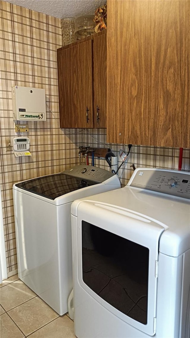 clothes washing area with light tile patterned floors, cabinets, a textured ceiling, and independent washer and dryer