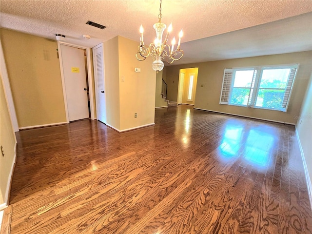 spare room featuring a textured ceiling, dark hardwood / wood-style floors, and an inviting chandelier