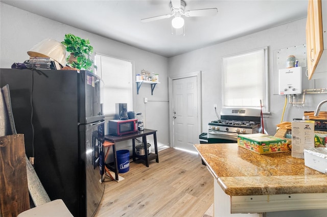 kitchen with light stone counters, ceiling fan, black appliances, tankless water heater, and light hardwood / wood-style floors