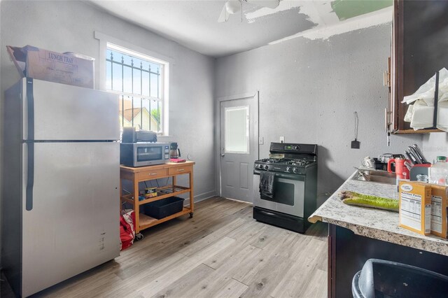 kitchen featuring ceiling fan, white refrigerator, black gas range oven, and light hardwood / wood-style flooring