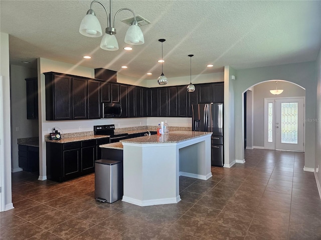 kitchen with an island with sink, hanging light fixtures, stainless steel appliances, light stone countertops, and a textured ceiling