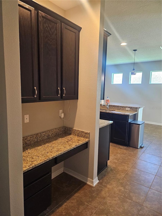 kitchen featuring light stone counters, dark brown cabinetry, sink, and pendant lighting