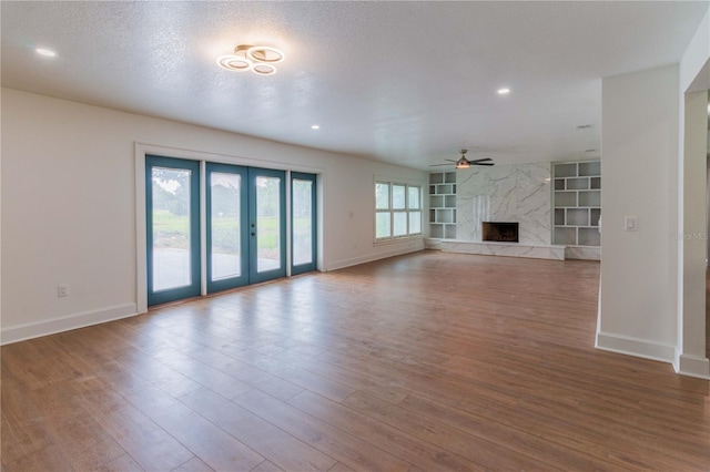 unfurnished living room with built in shelves, ceiling fan, french doors, a premium fireplace, and a textured ceiling