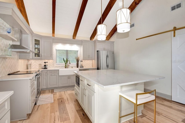 kitchen with a kitchen island, pendant lighting, vaulted ceiling with beams, stainless steel appliances, and light stone countertops