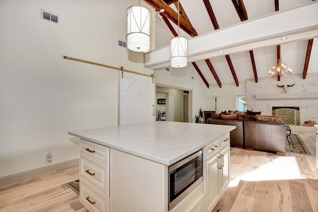 kitchen with stainless steel microwave, hanging light fixtures, a barn door, and beamed ceiling