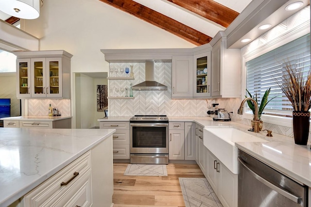 kitchen featuring lofted ceiling with beams, sink, light stone counters, stainless steel appliances, and wall chimney exhaust hood