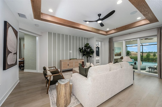 living area featuring light wood-style floors, visible vents, and a raised ceiling