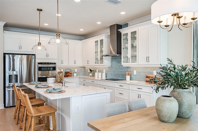 kitchen featuring wall chimney range hood, sink, stainless steel appliances, an island with sink, and white cabinets