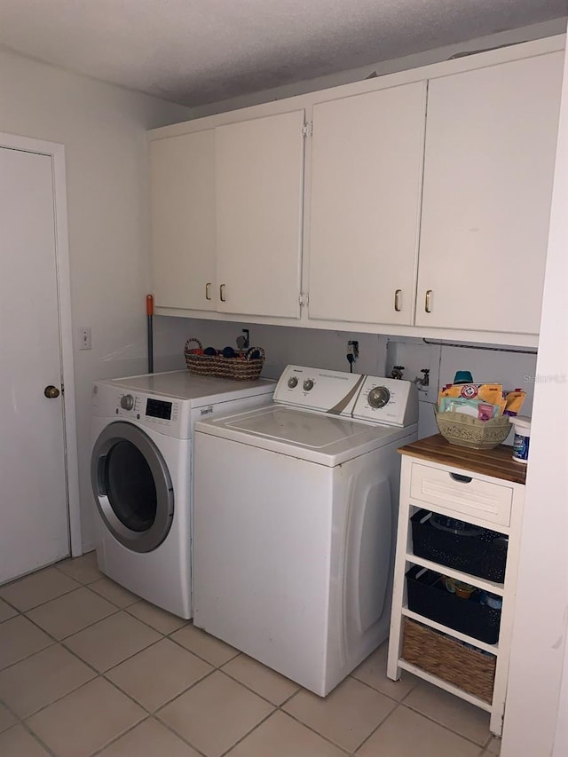 washroom featuring washing machine and clothes dryer, cabinets, and light tile patterned floors