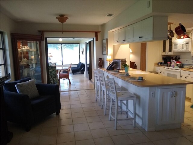 kitchen featuring white cabinets, light tile patterned floors, white appliances, kitchen peninsula, and a kitchen breakfast bar